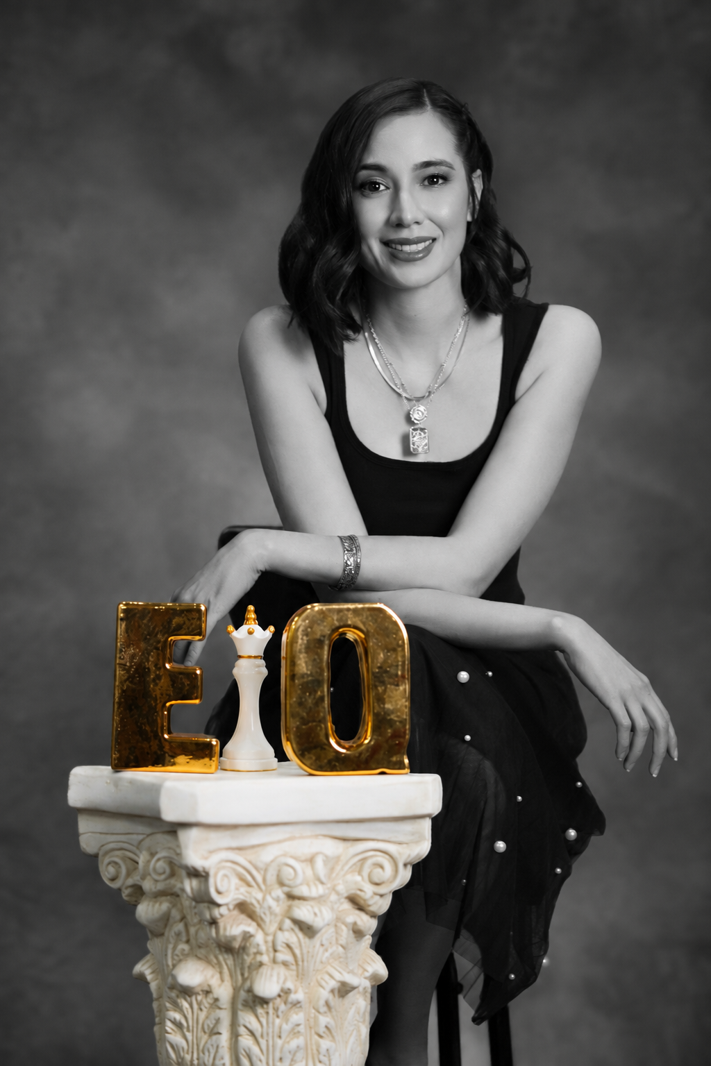 Portrait of Kar Anderson, Certified Emotional Intelligence Coach, seated beside gold EQ letters and a white chess queen on a marble pedestal